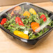 A Sabert black square catering bowl filled with salad on a counter.