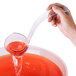 A hand using a Fineline clear plastic ladle to pour red liquid into a bowl.