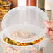 A close-up of a hand holding a Cambro translucent plastic food storage container with pasta inside.