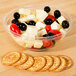 A close up of a Sabert clear bowl filled with cheese, crackers, and grapes.