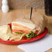 A sandwich wrapped in Bagcraft Packaging EcoCraft deli paper with chips on a plate.