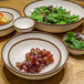 A white melamine oval platter with a brown rim on a table with bowls of fruit and salad.