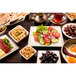 A white square melamine bowl filled with food on a table full of various food and drinks.