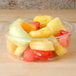 A bowl of fruit in a Bare by Solo clear plastic deli container on a table.