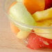 A clear Bare by Solo deli container filled with sliced red and yellow fruit on a wood surface.