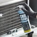 A person in black gloves using Noble Chemical Tech Line No Rinse Evaporator Coil Cleaner on a metal surface.