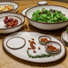 A table with bowls of cream and brown glazed melamine bowls filled with green salad, grapes, and nuts.