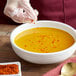 A gloved hand sprinkling Regal Extra Hot Ground Cayenne Pepper into a bowl of soup.