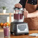 A man in an orange apron uses an AvaMix commercial blender to make a purple smoothie.