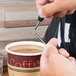A person using a Royal Paper Stix To Go black beverage plug to stir coffee in a cup.