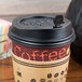 A close-up of a black Royal Paper Stix To Go beverage plug in a coffee cup with a lid.