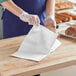 A person wearing gloves and an apron holding a Choice white bread bag.