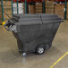 A large black Rubbermaid trash cart in a warehouse.