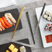A black plate of sushi with Acopa Heika gold stainless steel chopsticks.