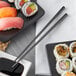 A white square plate with sushi rolls and a black liquid with a pair of Acopa stainless steel chopsticks.