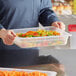 A person holding a Cambro translucent plastic container of vegetables.