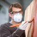 A man wearing a 3M face mask and goggles painting a wooden fence.
