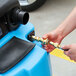 A person's hands holding a hose to a blue Mytee Grand Prix automotive extractor.