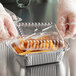 A person in a plastic glove putting fries in a Choice oblong foil take-out container with a dome lid.