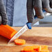 A person in black gloves using a Dexter-Russell paring knife to cut a carrot.