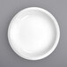 A close-up of a white International Tableware porcelain serving bowl with a white rim on a gray surface.