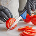 A person in black gloves using a Dexter-Russell scalloped utility knife to cut a tomato.