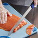 A person using a Dexter-Russell 360 Series slicing knife with a blue handle to cut a piece of fish.
