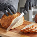 A person wearing black gloves uses a Dexter-Russell scalloped bread knife to slice bread on a cutting board.