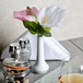 A white CAC European porcelain bud vase on a table with pink flowers in it.