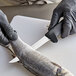 A person in black gloves using a Dexter-Russell narrow boning knife to cut a fish.