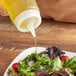 A person using a FIFO Innovations Precision Tip squeeze bottle to pour yellow liquid onto a salad.