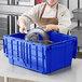 A woman in a chef's uniform putting a metal object in a blue Orbis tote box with a hinged lid.