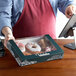 A man holding a Auto-Popup Window Bakery Box with donuts on a counter.