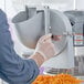 A person using a mixer attachment to shred carrots.