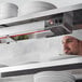 A chef in a white chef hat using a ServIt high wattage strip warmer on a shelf with plates.