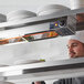 A chef in a professional kitchen looking at a ServIt strip warmer full of white plates.