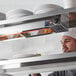 A chef in a professional kitchen using a ServIt 36" strip warmer to heat plates on a shelf.