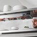 A man using a ServIt high wattage strip warmer to heat plates in a professional kitchen.