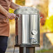 A man using a Backyard Pro stainless steel brewing pot stand to hold a large metal container.