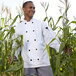 A man wearing a Uncommon Chef long sleeve white chef coat standing in a corn field.