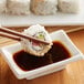 A pair of chopsticks holding a sushi roll over a white square dish with Lee Kum Kee soy sauce.