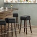 A Lancaster Table & Seating Sofia vintage wood backless bar stool with a black vinyl seat.