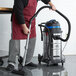 A man in a red apron using a Lavex stainless steel wet/dry vacuum to clean a professional kitchen.