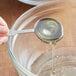 A hand using a spoon to pour golden liquid from a Golden Barrel Organic Medium Invert Sugar pail into a bowl.