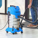 A man using a Lavex stainless steel wet/dry vacuum to clean a floor in a professional kitchen.