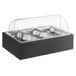A wooden display stand with black and silver Vollrath food pans and a clear roll top cover.