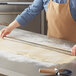 A person using an Ateco stainless steel rod to cut dough on a table.