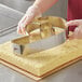 A gloved hand uses an Ateco Stainless Steel Number 6 / 9 cutter to cut a cake.
