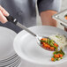 A person using a Vollrath stainless steel perforated basting spoon to serve vegetables on a plate.