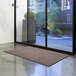 A brown Lavex Olefin entrance mat in front of glass doors.
